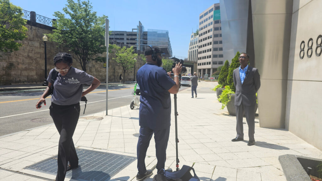 Documentarian, and Founder/Director of the Peoples Justice Council, Michael Malcom sets up a tripod to interview Pastor Timothy Williams of Shiloh Community Center. Pastor Williams, daughter and Shiloh Community Center Executive Assistant, Melissa Williams walk to the left of Michael Malcom.